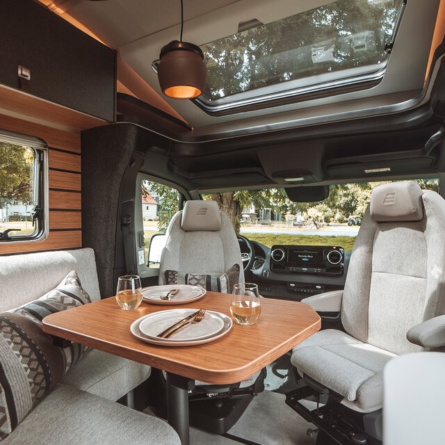 Der Tisch des Wohnbereichs im HYMER ML-T ist gedeckt. Die Multifunktionsleuchte wurde über dem Tisch montiert.
