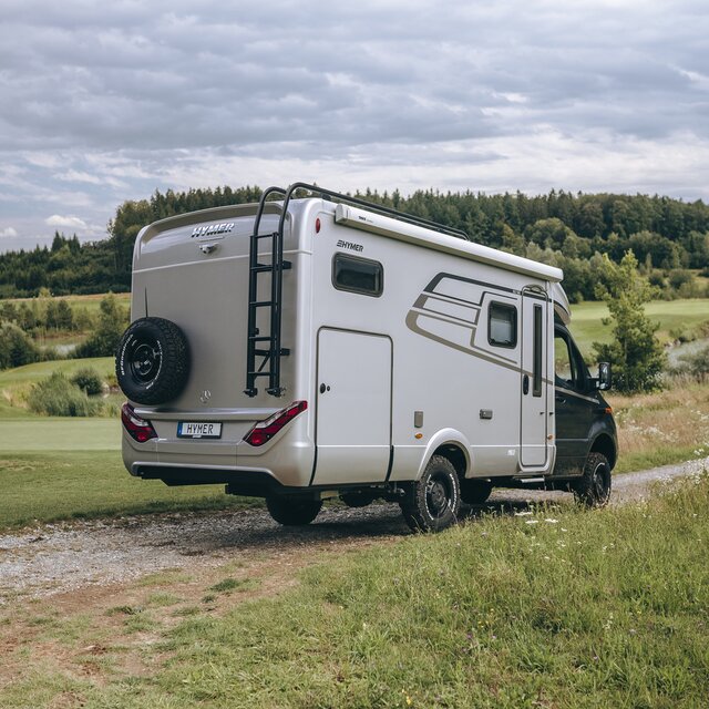 Der HYMER ML-T ist von hinten zu sehen, wie er auf einem Feldweg zwischen zwei Wiesen steht.