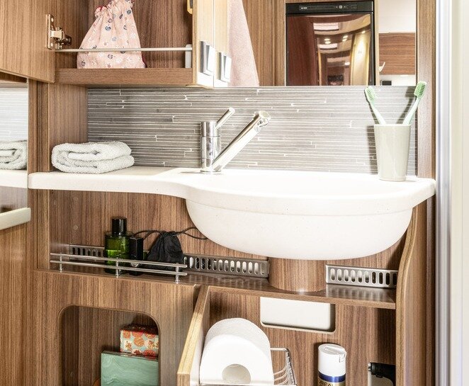 Wastafel met tandenborstelbeker en opbergvakken rondom gevuld met badkamerbenodigdheden in de HYMER ML-T