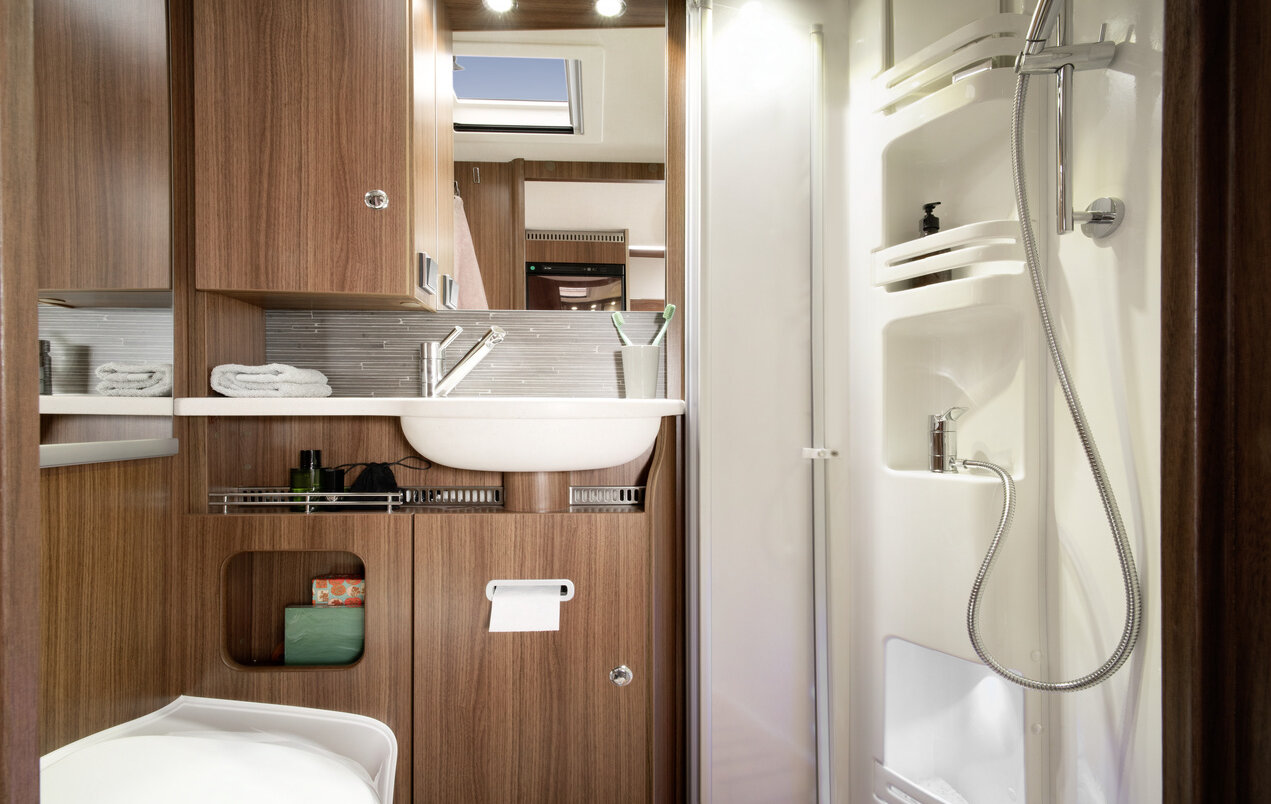 Comfortbadkamer in de HYMER ML-T: douchecabine met houten lattenbodem, wastafel, spiegel, toilet, opbergkasten