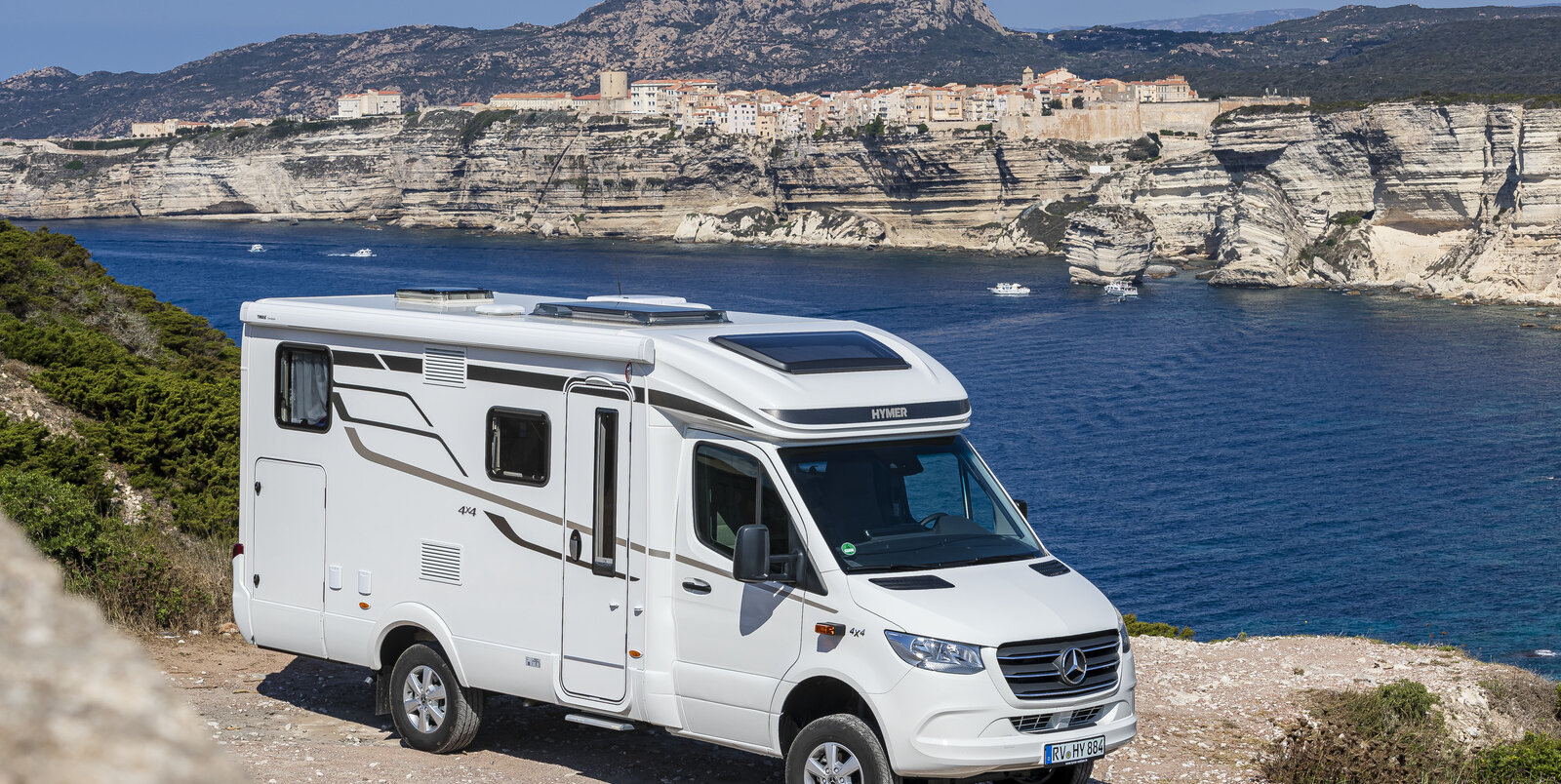 HYMER ML-T 570 in front of the sea mouth with azure blue water and rock formation with houses on the other bank