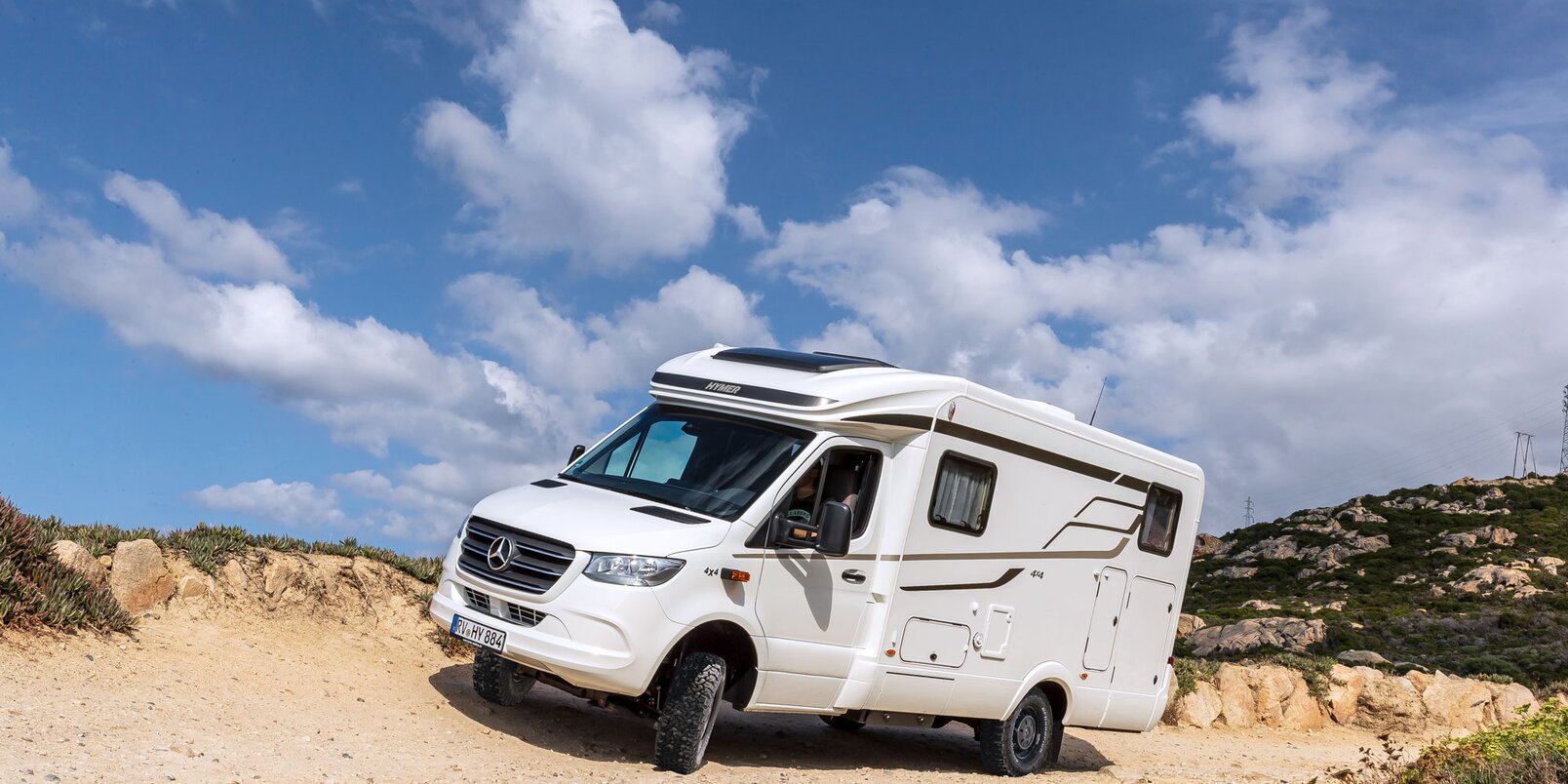 HYMER ML-T in an inclined position in coarse gravel, sandy terrain with rock formations and a blue sky with white clouds