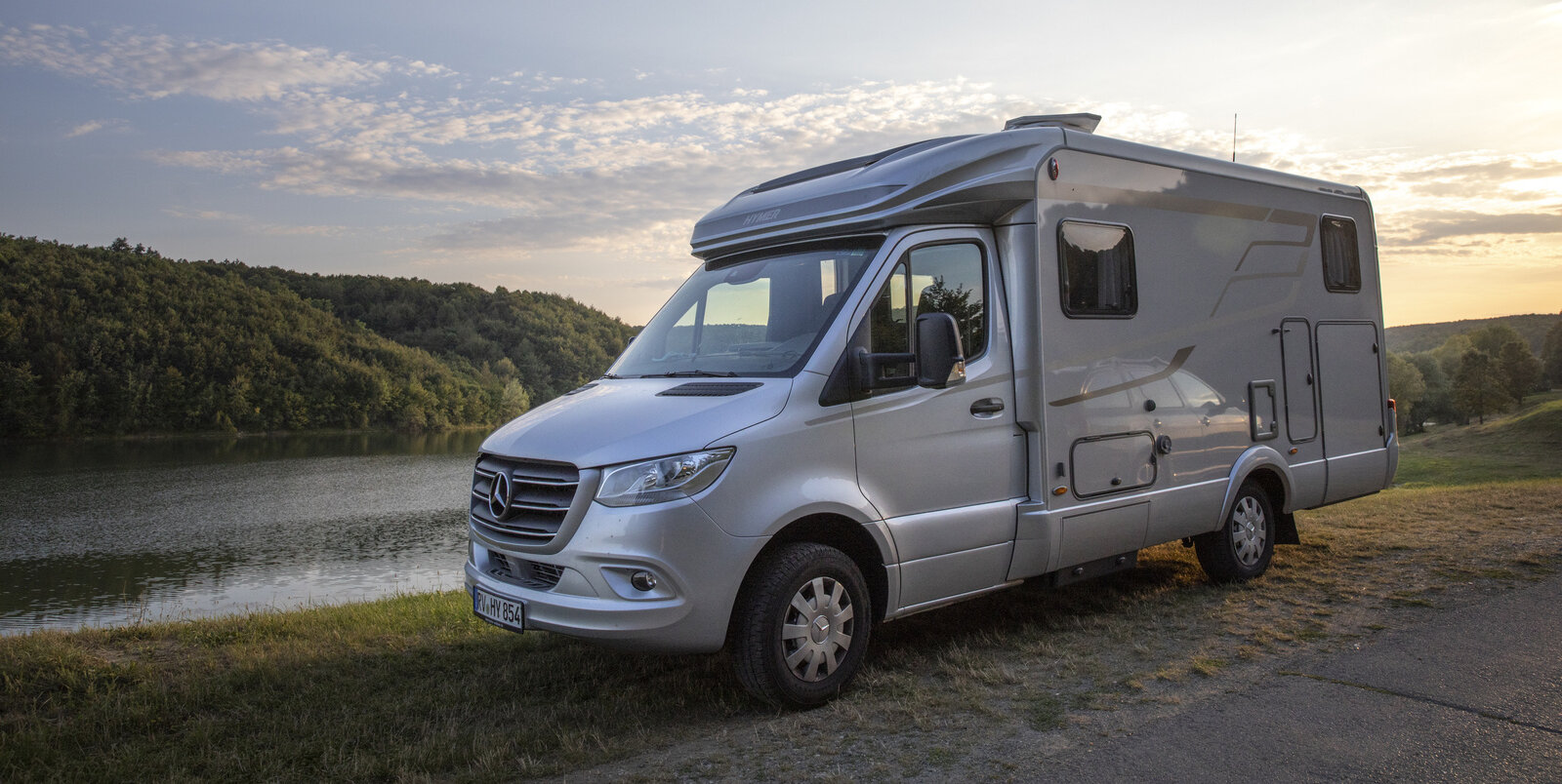 HYMER ML-T 580 in a Mercedes standing on hard shoulder by a body of water with a forest on the other bank