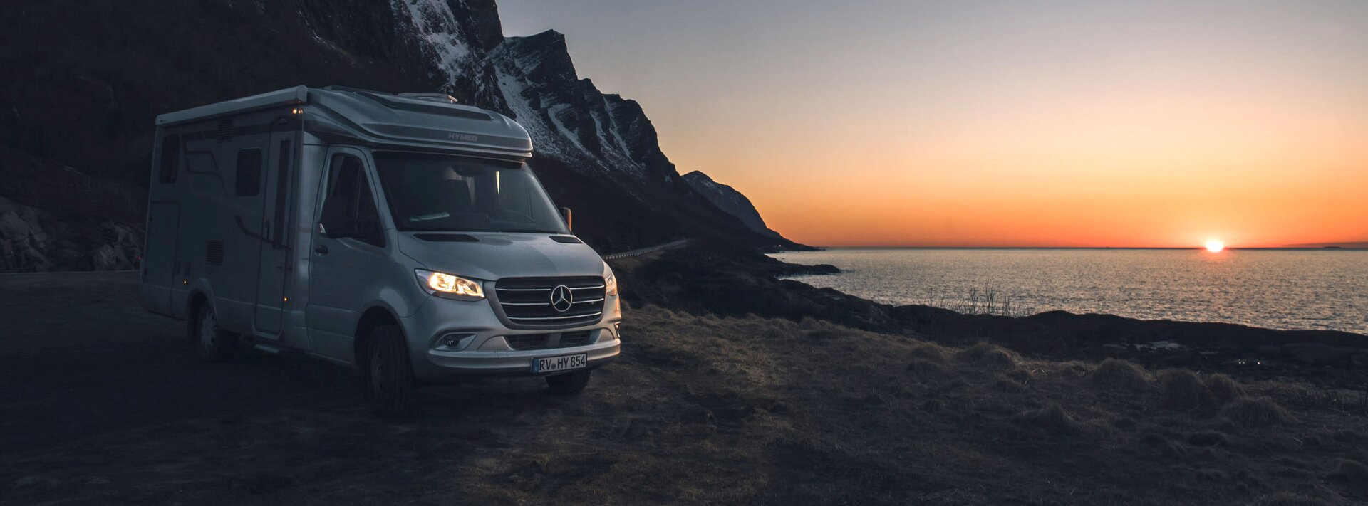 Semi-integrated HYMER motorhome based on Mercedes at sunset on the beach with cliffs