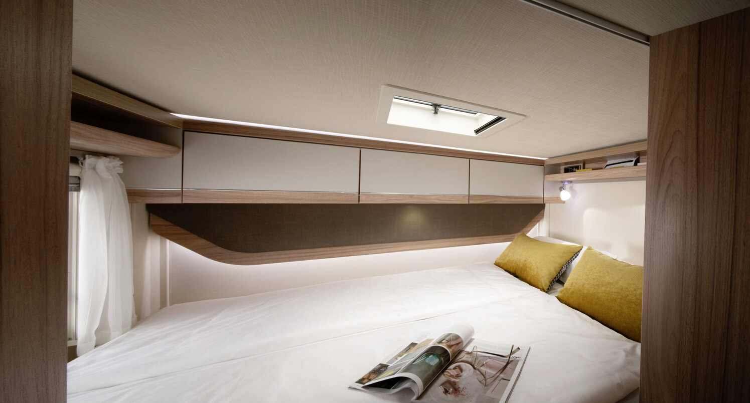 Covered rear bed, two yellow decorative pillows and overhead storage cupboards in the HYMER ML-T motorhome
