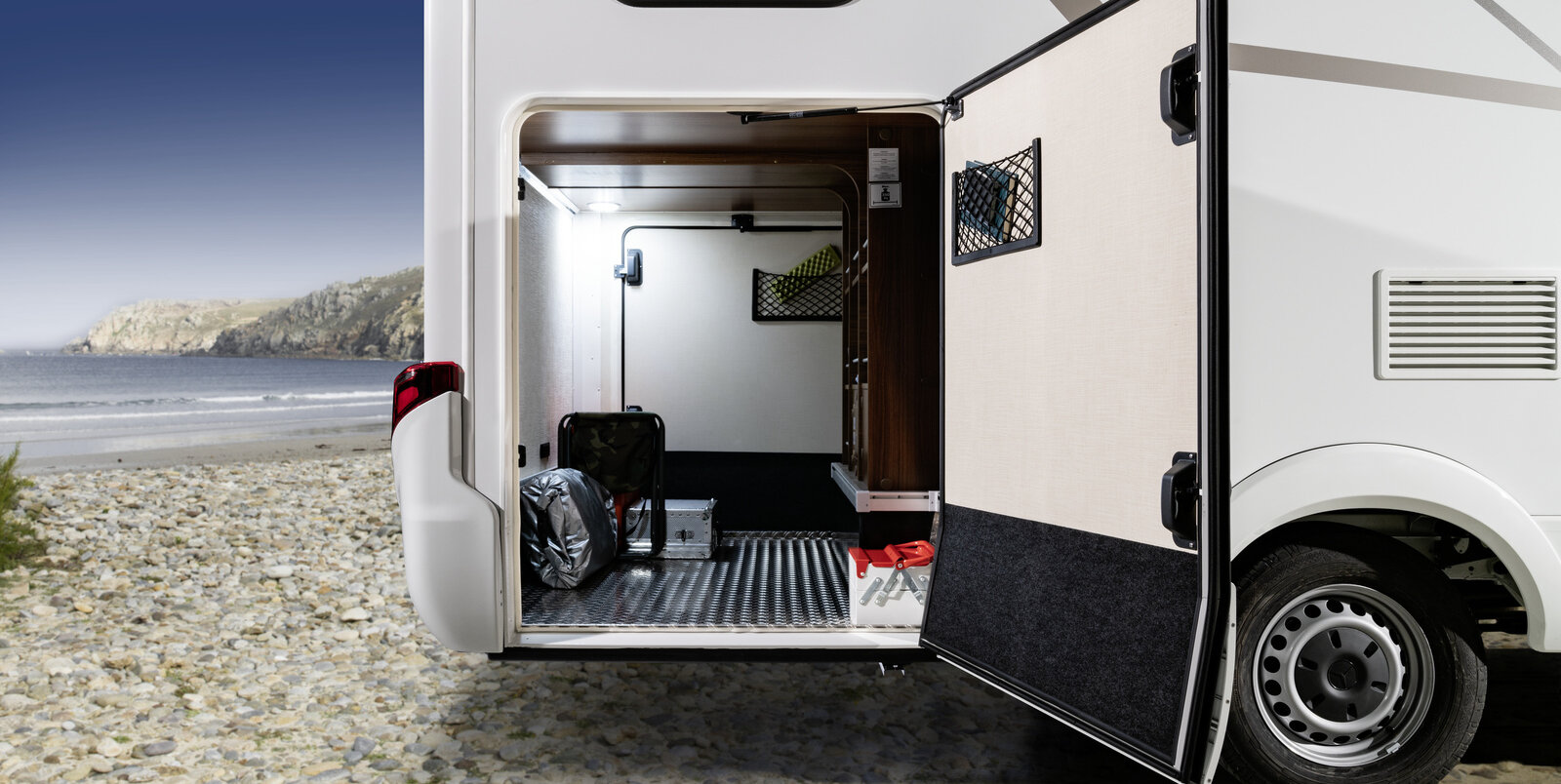 The door of the rear garage of the Wonmobil HYMER ML-T, which is loaded with travel accessories, is open to the right in the direction of travel