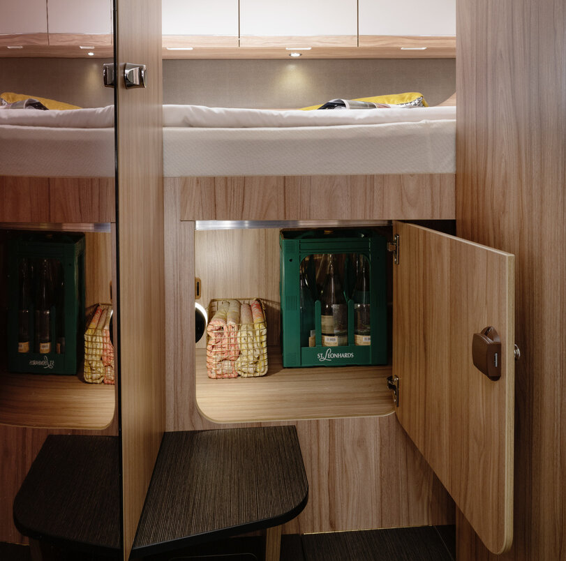 Open storage compartment with water box and other utensils under the transverse bed in the rear of the HYMER ML-T 560
