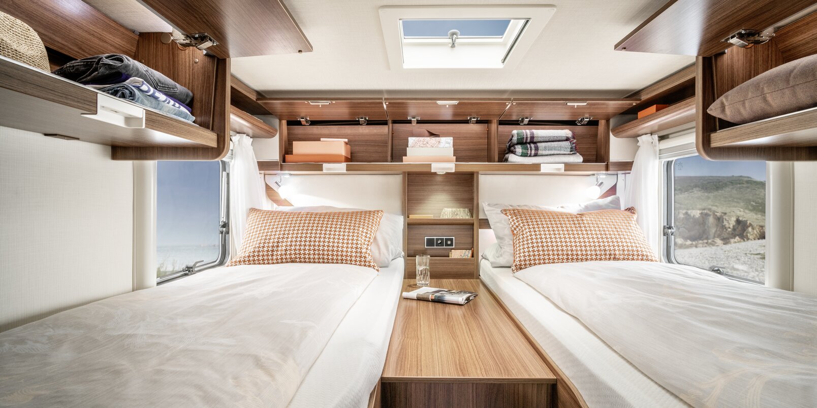 Two made up lengthways single beds, central access, all-round open overhead storage cupboards filled with utensils in the HYMER ML-T