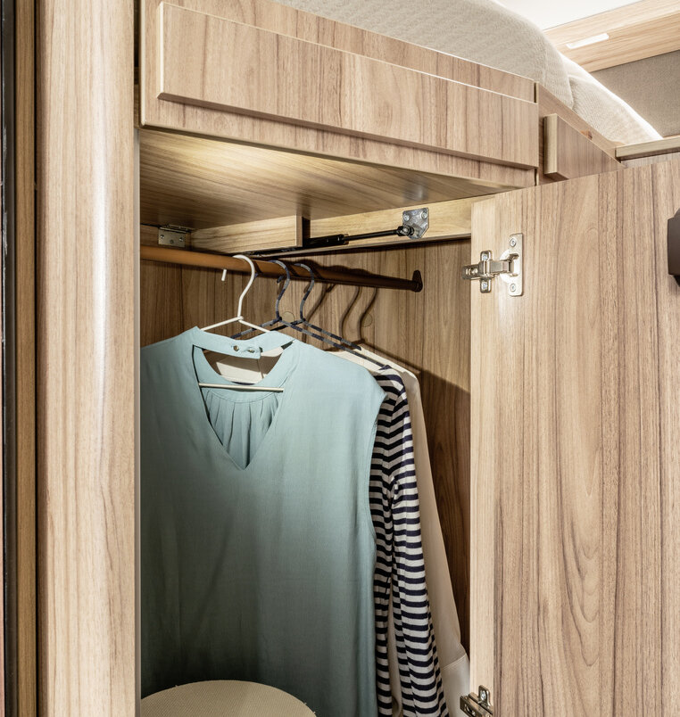 Open, illuminated wardrobe with hangers on the rail under the bed in the rear of the HYMER ML-T