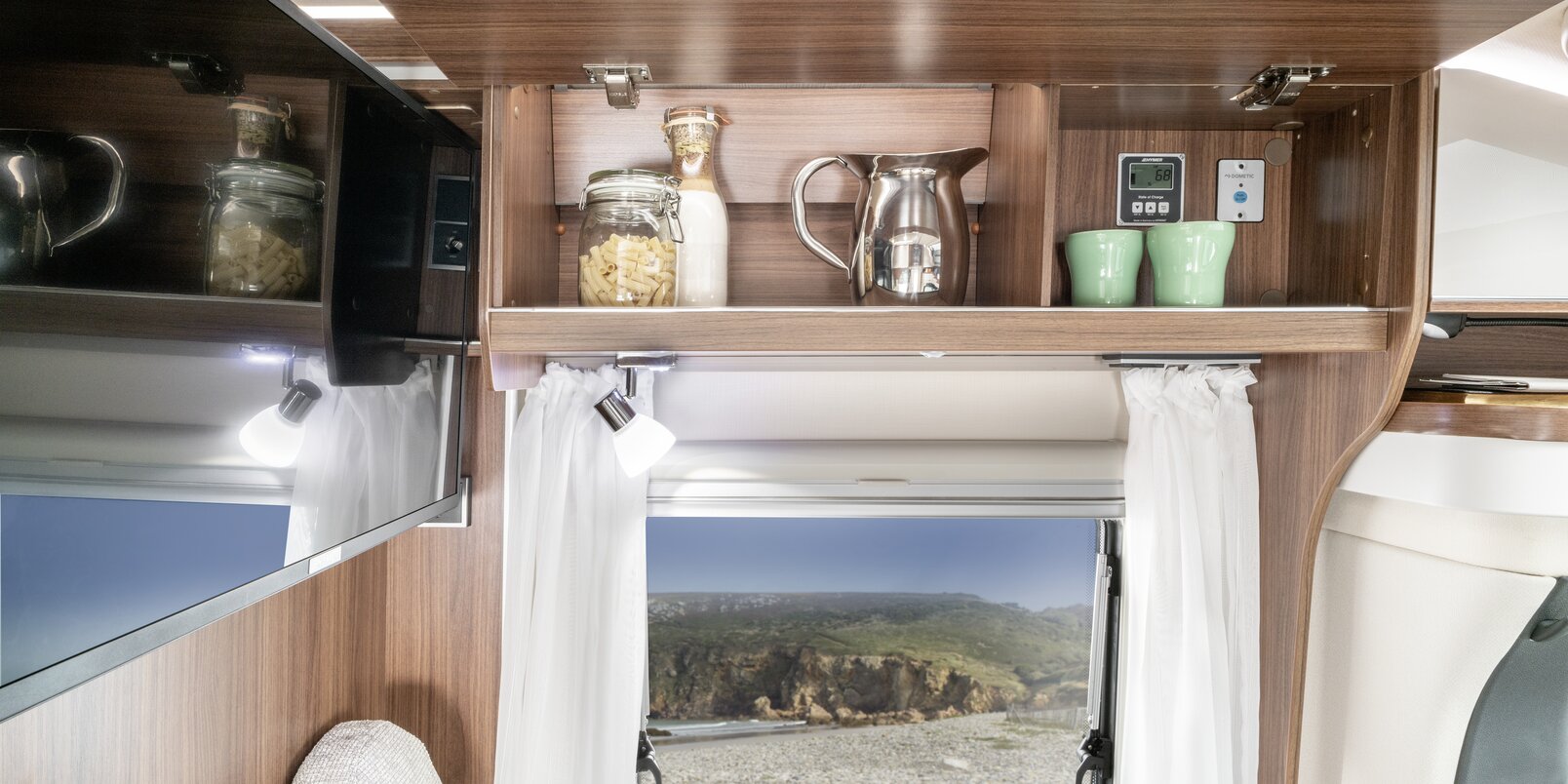 Open overhead locker filled with kitchen accessories under the seating area, underneath the side wall window on the HYMER ML-T