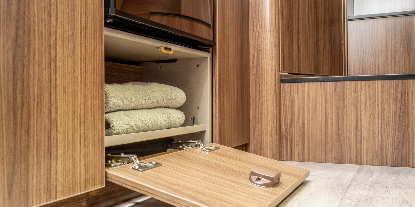 Small storage compartment filled with towels below the refrigerator in the HYMER ML-T 580