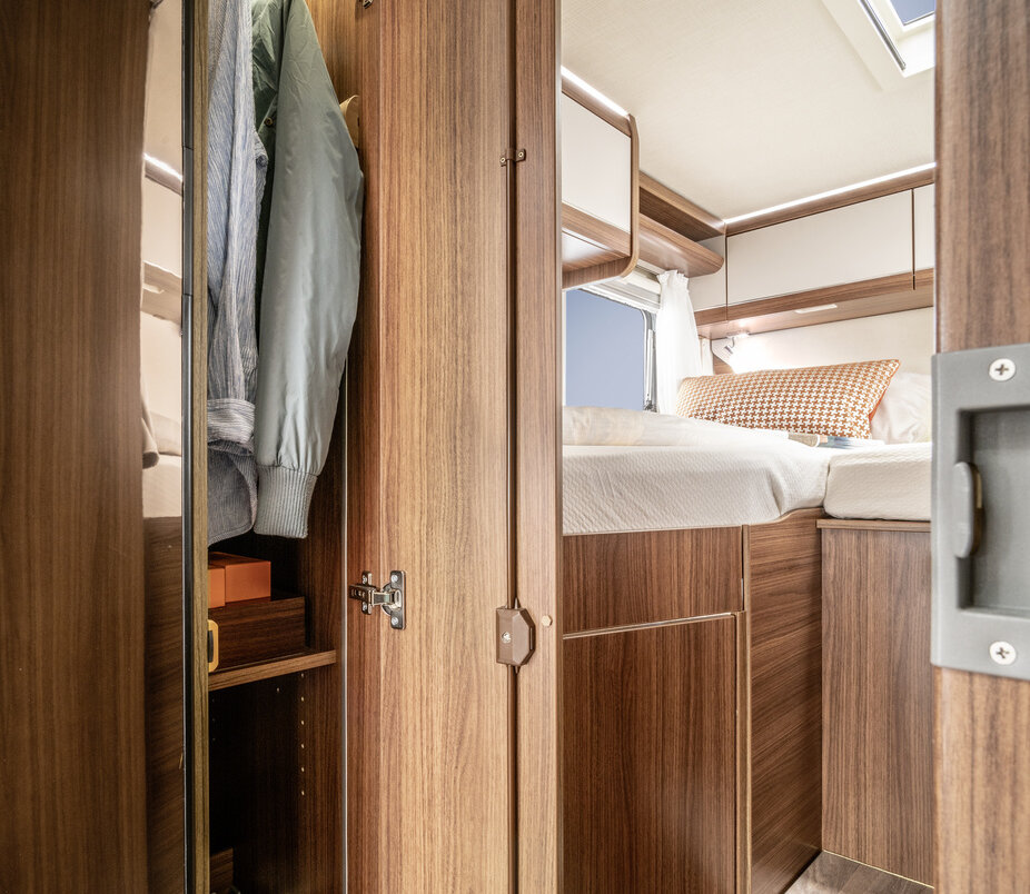 Open, floor-to-ceiling wardrobe with a filled clothes rail and storage compartments as well as a covered lengthways single bed in the HYMER ML-T