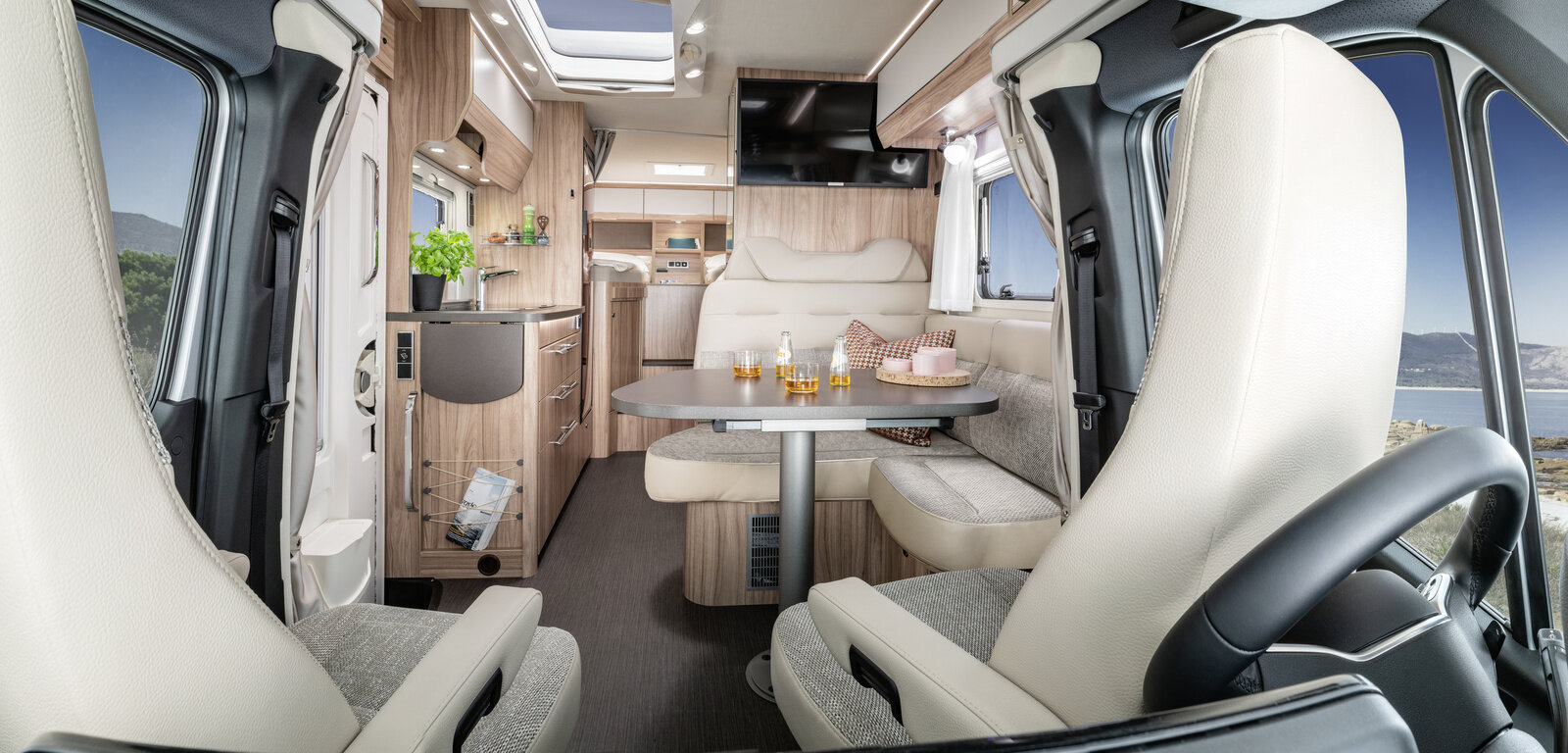 Bright living room in the HYMER ML-T 570 with driver's seats, seating area, plasma TV, entrance door, kitchen block and sleeping area