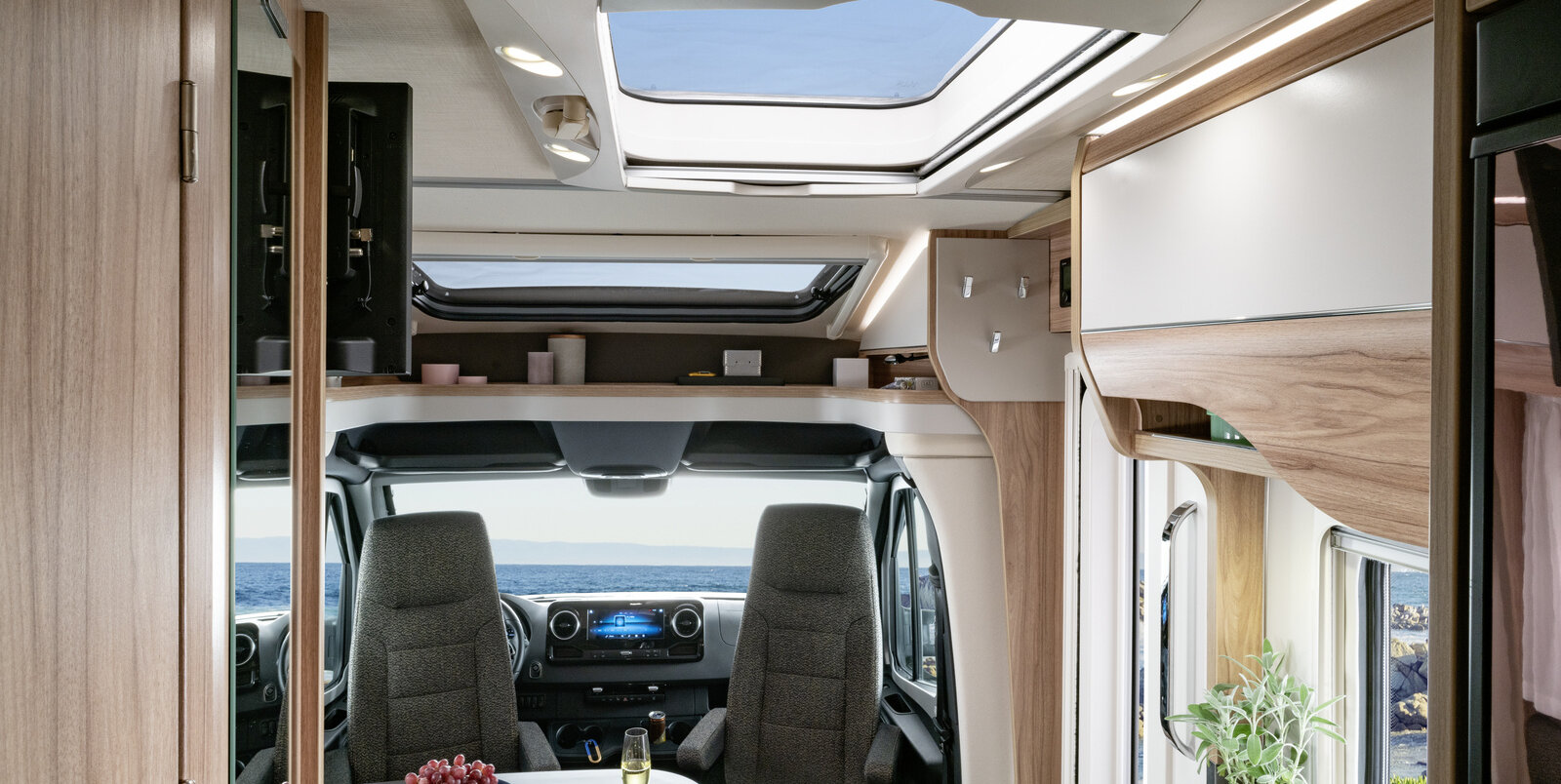 Living space in the HYMER ML-T: set table, entrance door, panoramic roof vent, driver's seats, storage board above driver's seats