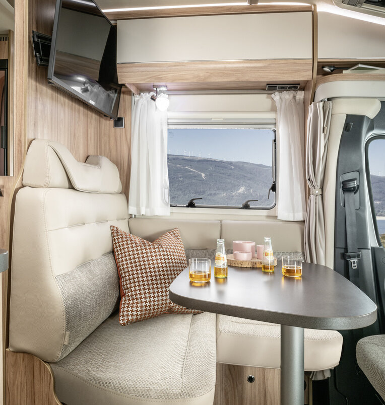 Living area in the HYMER ML-T 570: bright seating area, laid table, flat screen TV, side window and overhead storage cupboard