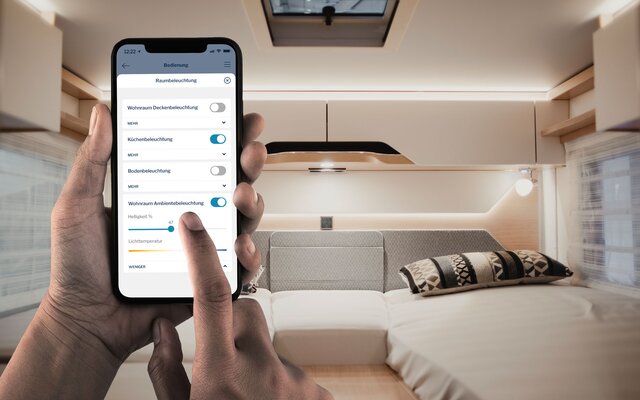 Hendene til en person som bruker en mobiltelefon i baksoveområdet av en bobil, skjermen viser bruken av HYMER Connect-appen