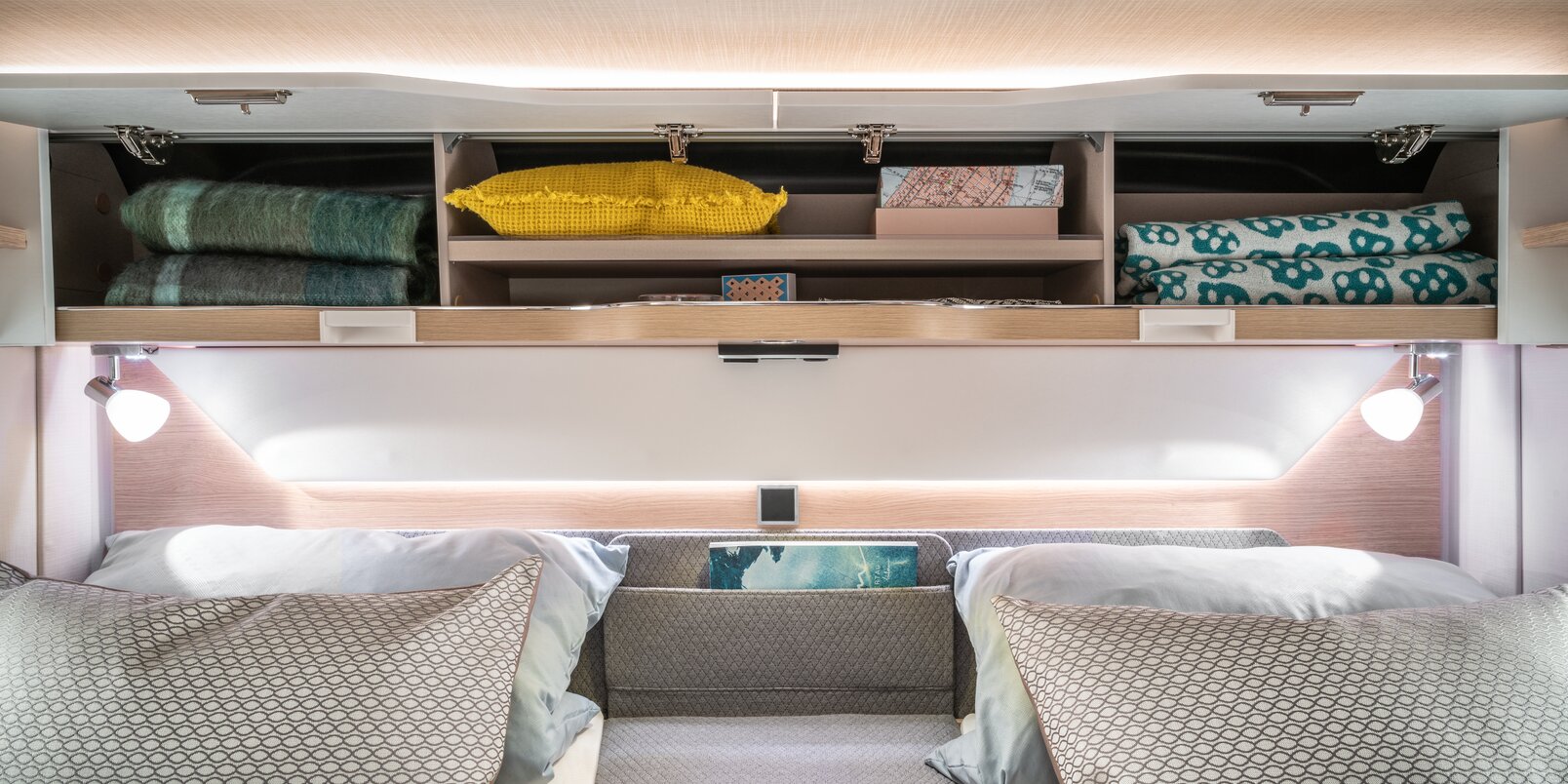 Open, filled overhead lockers above the rear bed, bed lighting, utensil pocket and pillow in the HYMER B_MC I WL