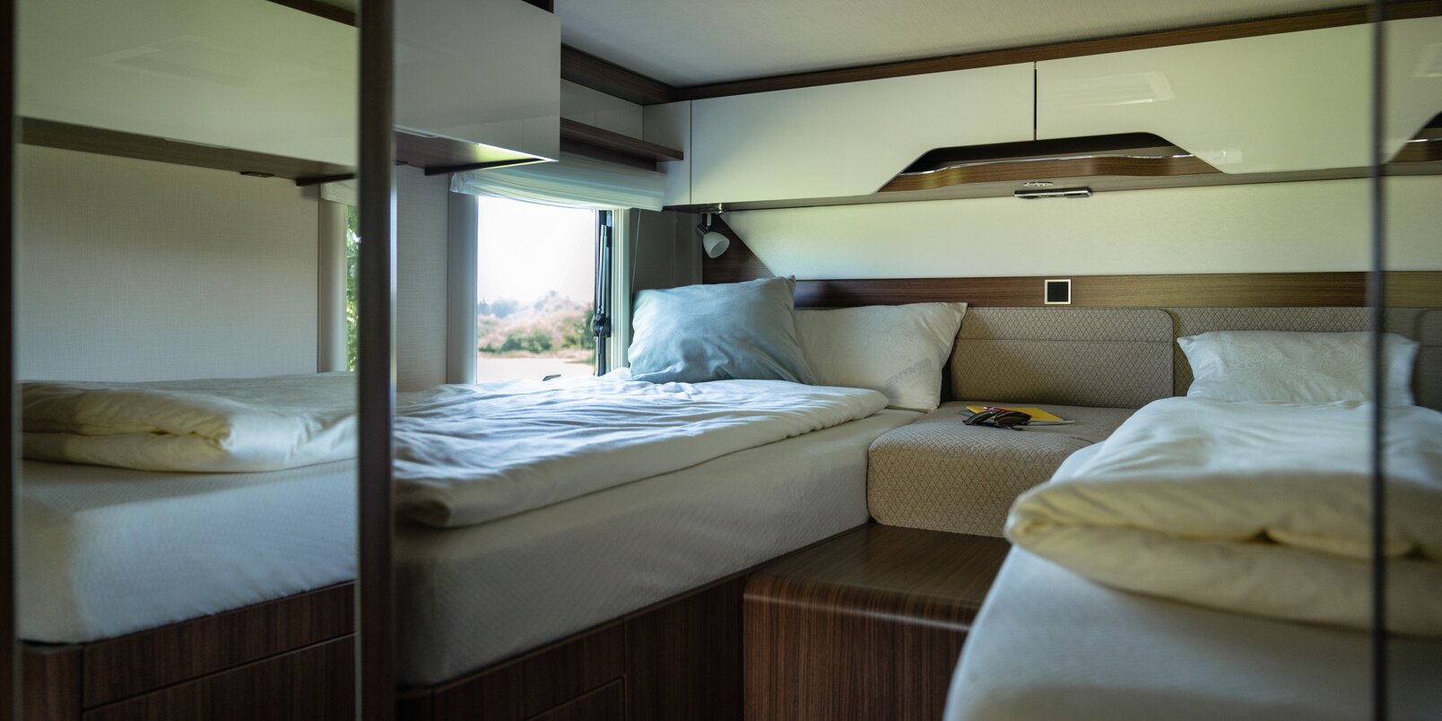 Bedroom with made up lengthways single beds, center console and overhead storage cupboards in the rear of the HYMER B ModernComfort WhiteLine