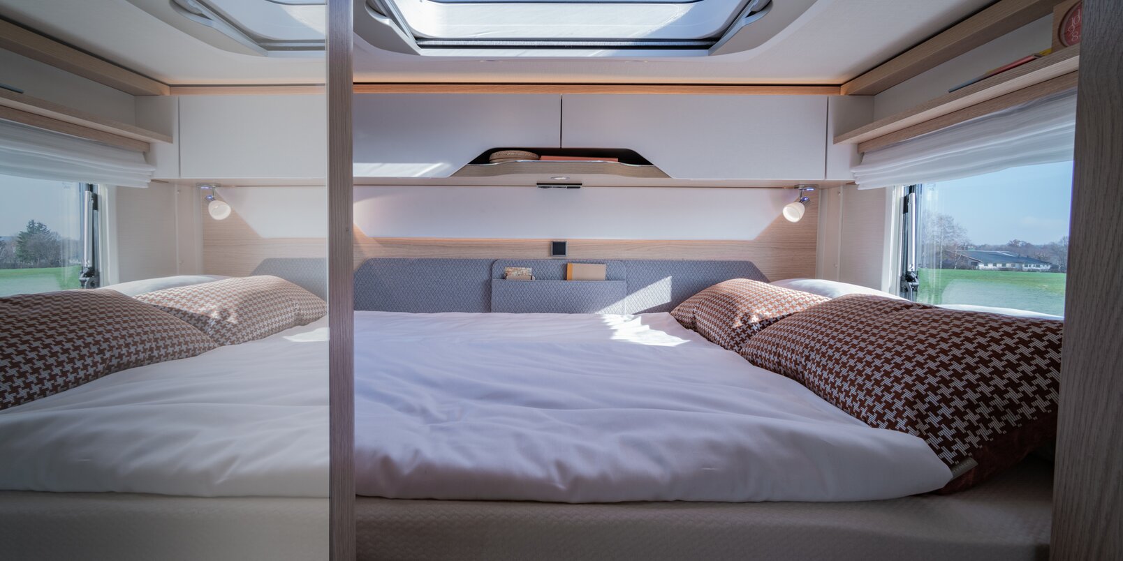 Sleeping area in the HYMER B-MC T WhiteLine: covered rear bed, overhead storage cupboards, side and roof windows, reading lights