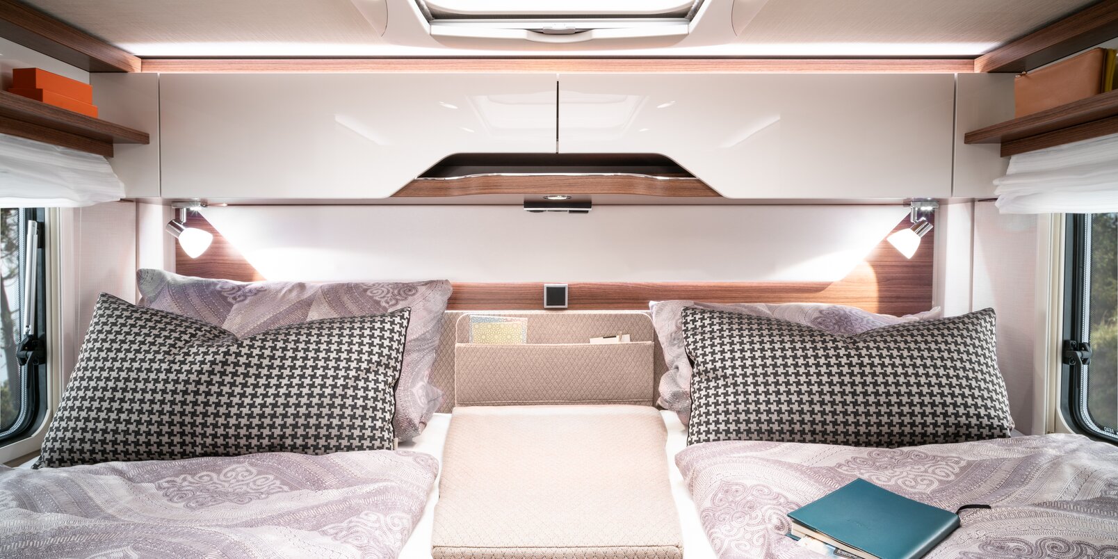 Covered lengthways single beds, central additional cushions, lighting, overhead storage cupboards and reading material in the rear of the HYMER B-MC T WL