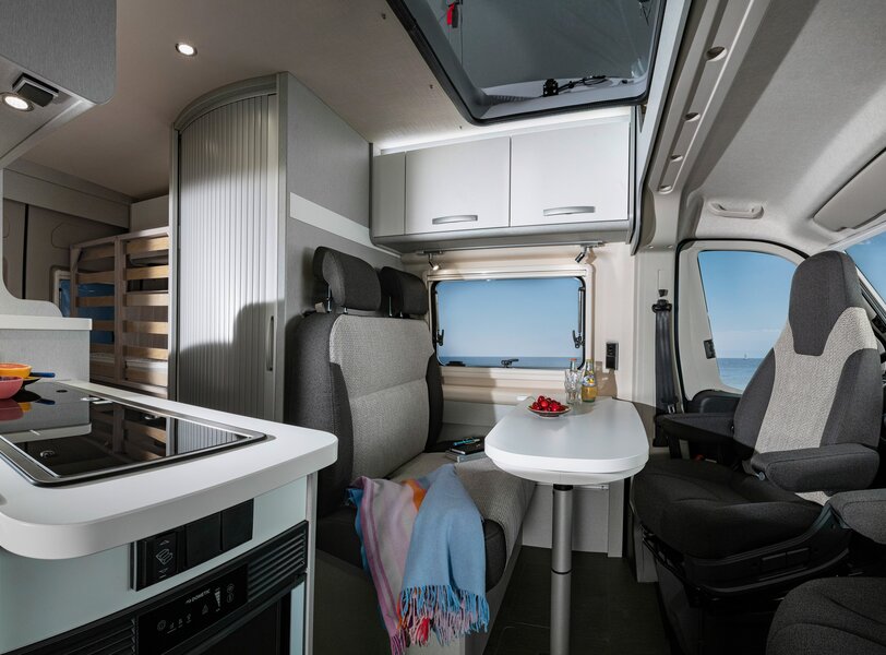 Interior del HYMER Free 540 Blue Evolution: zona de estar con mesa y asientos del conductor, bloque de cocina, baño y zona trasera