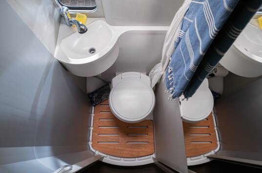 Toilet, wastafel, houten lattenbodem, roldeur en badhanddoeken in de compacte badkamer van de HYMER Free 540 Blue Evolution