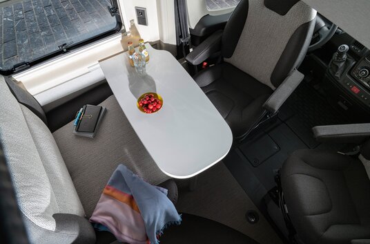 Seating group in the HYMER Free 540 Blue Evolution with drinks and fruit bowl on the table, notebook and blanket on the bench