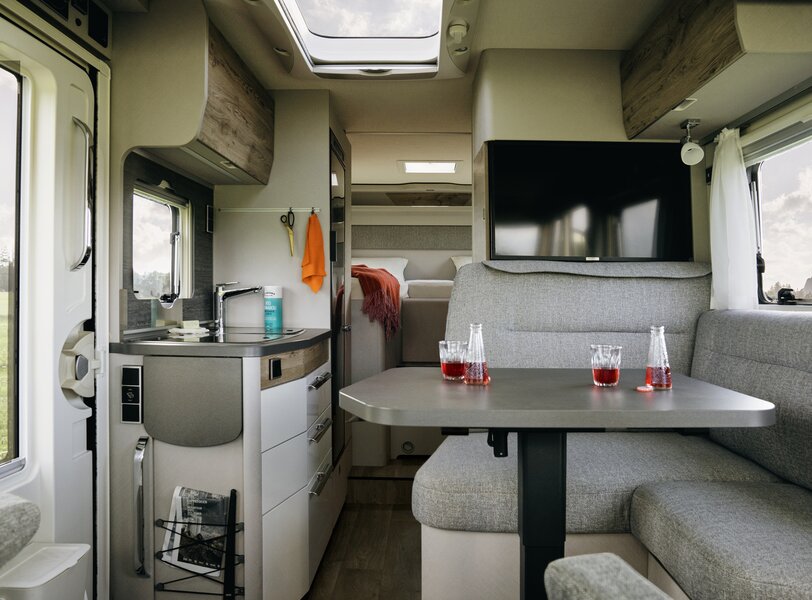 Interior of the HYMER Exsis 580 Pure: seating area, flat screen TV, entrance door, kitchen block, sleeping area