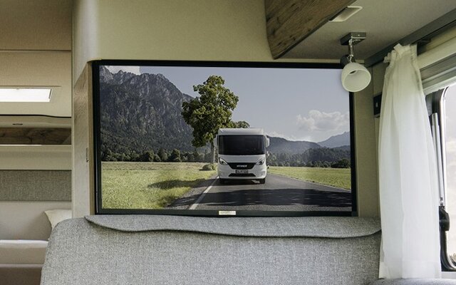 Back seat of the seating group and above it TV plasma with background image Hymermobil in nature in the Exsis 580 Pure