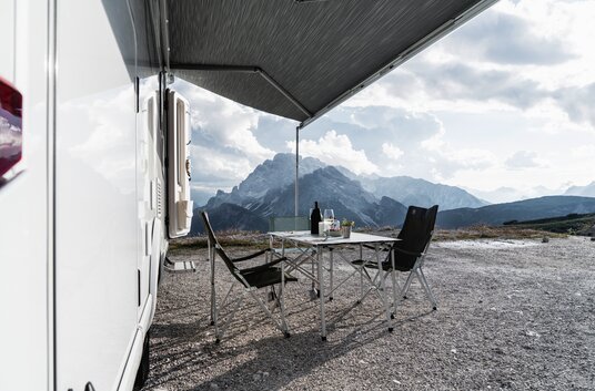 Camping furniture under the awning of the HYMER Exsis-t 580 Pure with a panoramic view of the Alps