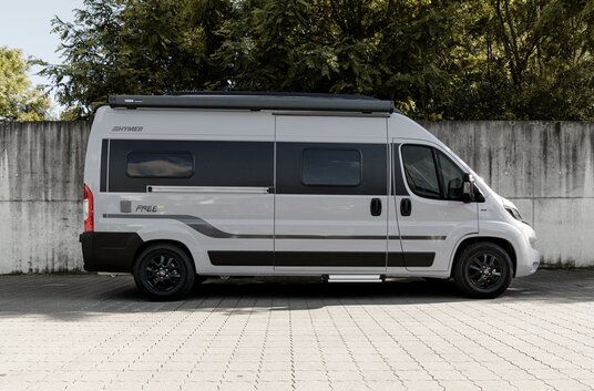 Parked HYMER Free 600 Campus in front of a concrete wall with tall trees behind