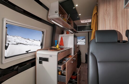 Interior in the HYMER Grand Canyon S CrossOver: bench, kitchen area with open, filled drawers and overhead storage cupboards