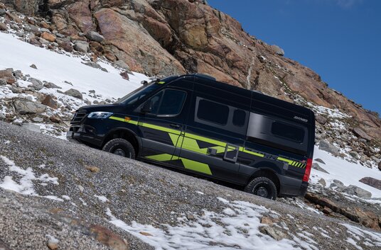 HYMER Grand Canyon S CrossOver driving uphill on gravel in the mountains with residual snow
