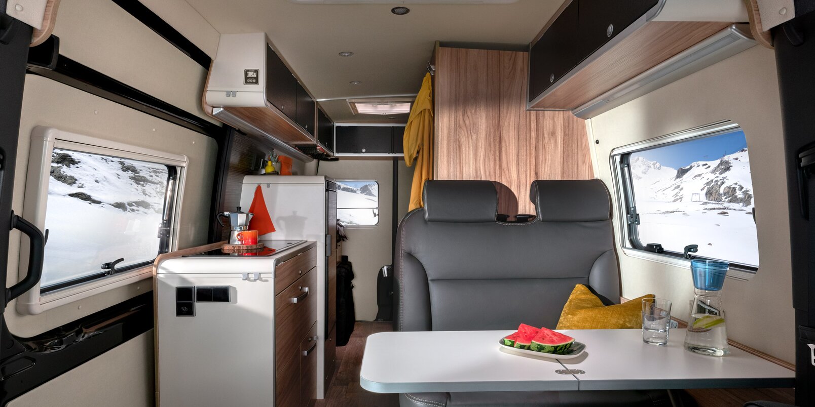 Interior in the HYMER Grand Canyon S CrossOver: seating group with occupied table, kitchen area, rear area
