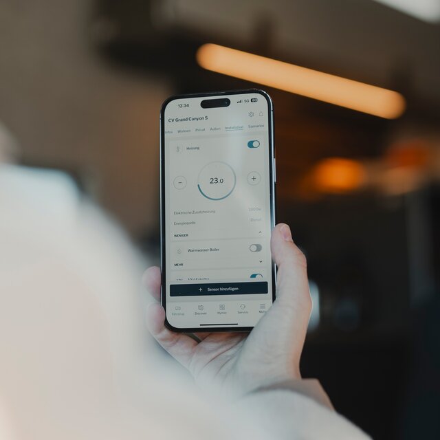 Person, die auf ihrem Handy die HYMER Smart Connect App benutzt und dabei in einem Camper Van sitzt