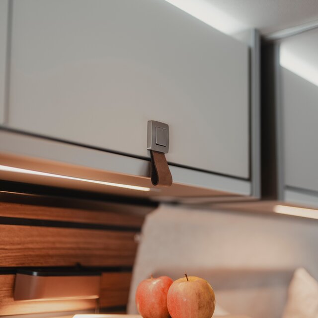Heller Dachstauschrank mit brauner Lederschlaufe, am unteren Bildrand sieht man zwei Äpfel