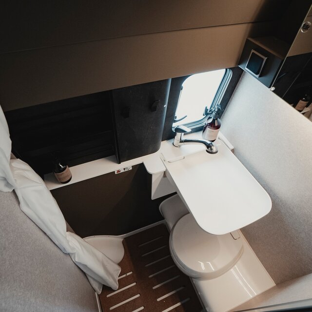 Badezimmer in einem Camper Van: Duschkabine mit Waschbecken, Kassettentoilette, Spiegel, Ablageschränke und Duschvorhang