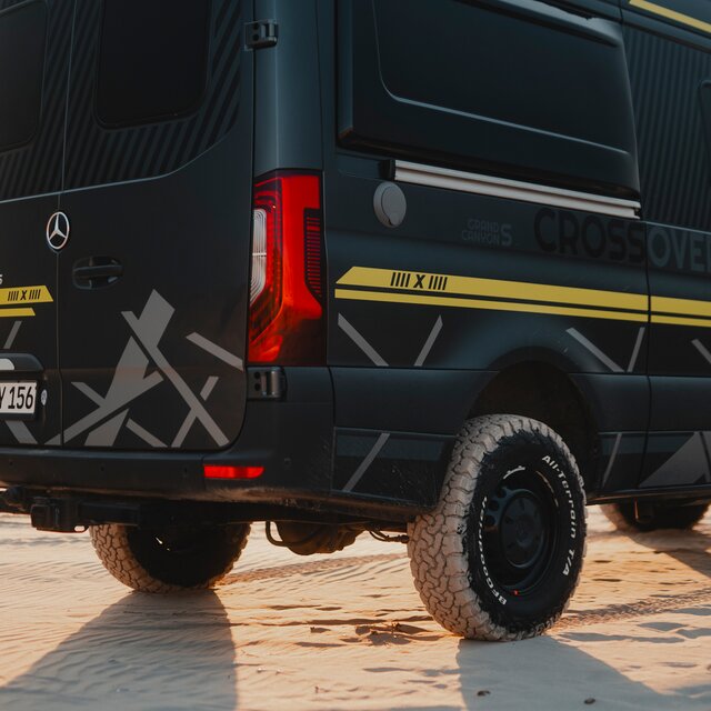 Seitenansicht Hinterachse eines Camper Vans mit schwarzen Felgen, All-Terrain Reifen, 4x4 Beklebung in Neon Grün