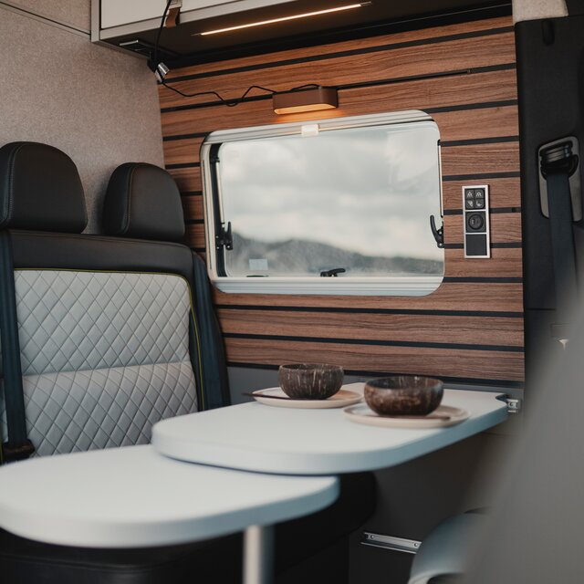Moderner Innenraum in einem Camper Van, Sitzgruppe mit gedecktem Tisch, im Hintergrund das Seitenfenster
