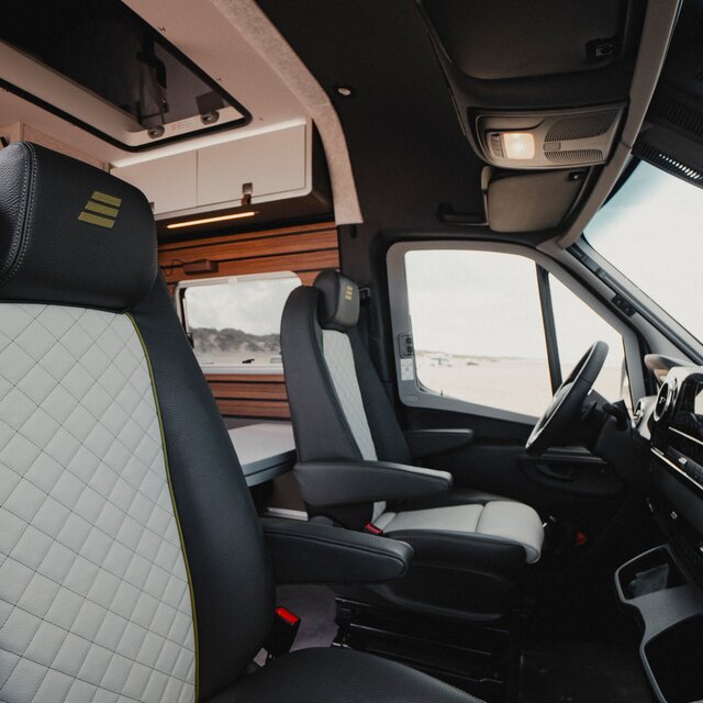 Fahrerhaus in einem Camper Van mit zwei Fahrersitzen in schwarz grauem Leder, schwarze Amaturen, schwarzes Lenkrad