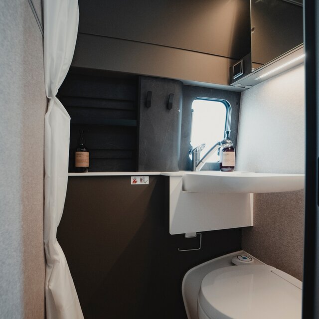 Badezimmer in einem Camper Van: Duschkabine mit Waschbecken, Kassettentoilette, Spiegel, Ablageschränke, Duschvorhang