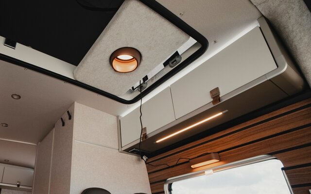 Dachstauschränke oberhalb der Sitzgruppe in einem Camper Van, sowie der offene Durchgang an der Decke der zum Schlafdach führt, in diesem Durchgang ist die Pendelleuchte in einer hellgrauen Halterung angebracht