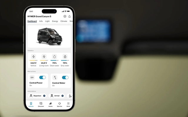 Affichage d'un écran de téléphone portable montrant le contenu d'une application pour contrôler un camping-car. Le téléphone est représenté devant un intérieur flou de camping-car.