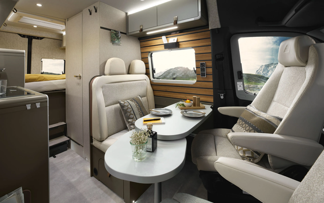Intérieur moderne d'un camping-car avec des garnitures claires, montrant le coin salon avec une table de séjour pivotée. Le mur du coin salon est revêtu de panneaux en bois.