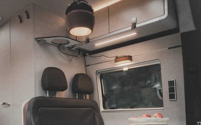 Vue sur la zone au-dessus d'un groupe de sièges dans un camping-car, où diverses sources lumineuses sont visibles sur, sous, au-dessus et devant un compartiment de rangement en hauteur.