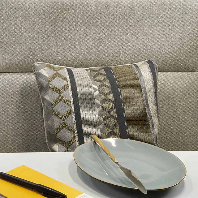 Gros plan d'un coussin aux motifs dans différentes teintes de gris, beige et vert olive.