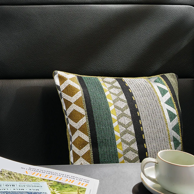 Gros plan d'un coussin aux motifs dans différentes teintes de beige, vert, jaune, marron et noir.