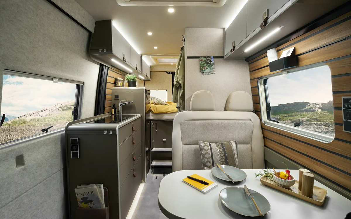 La vue à travers l'intérieur du HYMER Grand Canyon S dans le monde du style Ivy Green, de la zone de sièges à la zone de couchage.