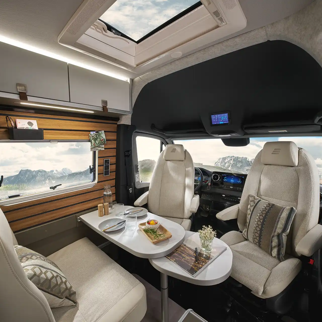 Le salon du HYMER Grand Canyon S dans le monde du style Ivy Green est visible depuis la cuisine. Derrière, la cabine de conduite est visible.