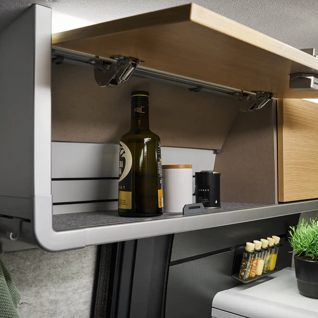 L'armoire de toit au-dessus de la cuisine du HYMER Grand Canyon S dans le monde du style Pearl Grey est ouverte. L'huile et les épices sont visibles à l'intérieur.